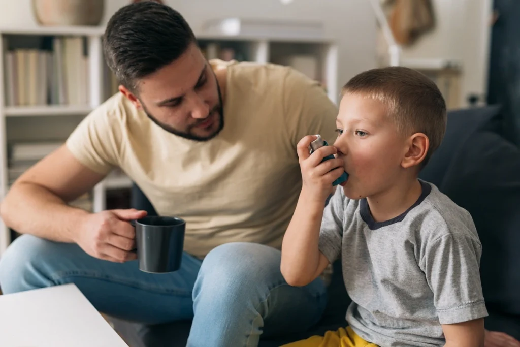 father watching his son use an inhaler for asthma
