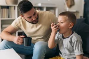 father watching his son use an inhaler for asthma